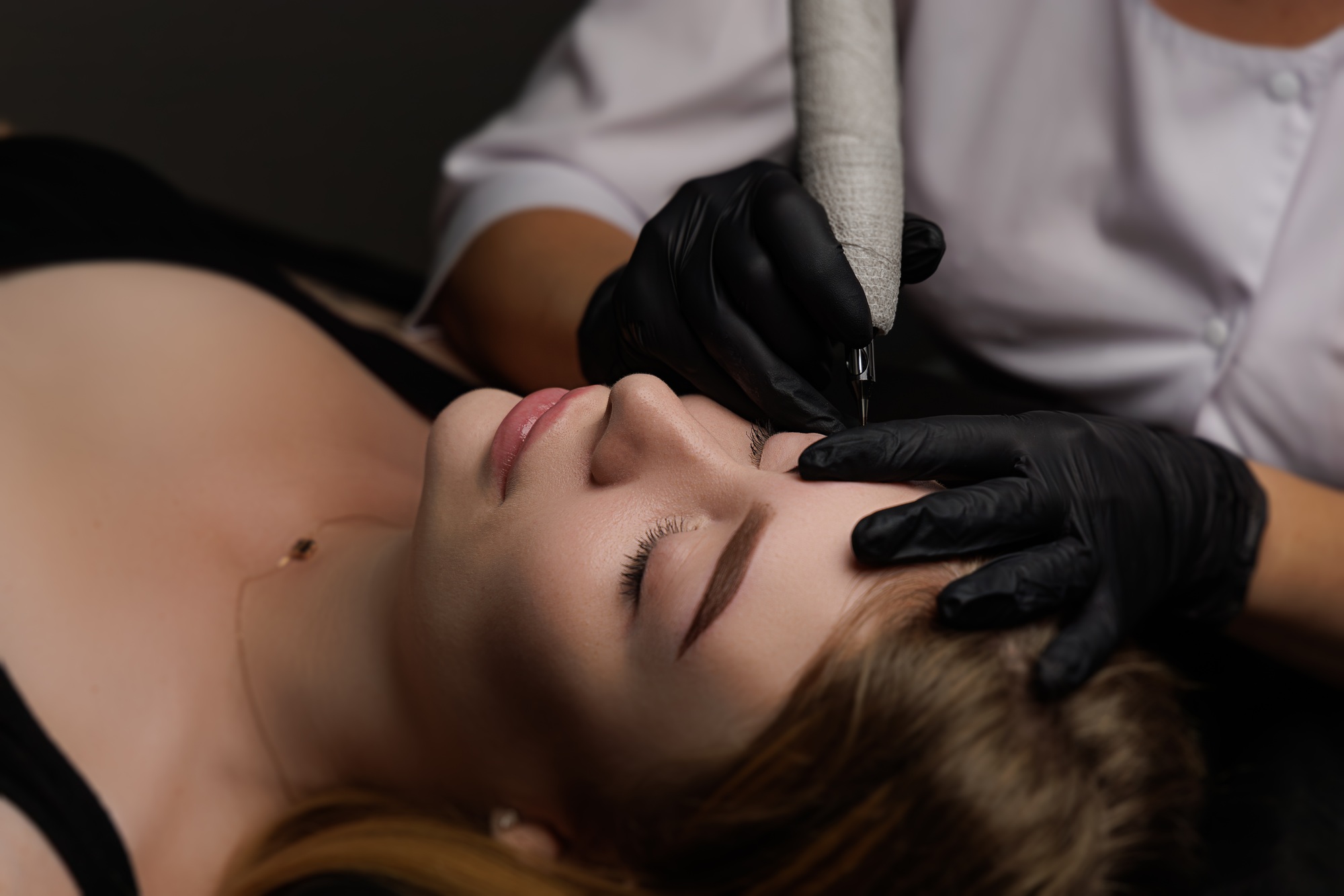 A girl of model appearance lies on the procedure of permanent eyebrow makeup experienced master