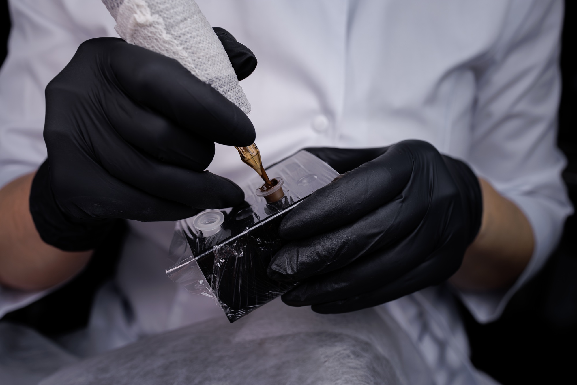 Close-up of the hands of the master, who holds a tattoo machine and dials pigment into it